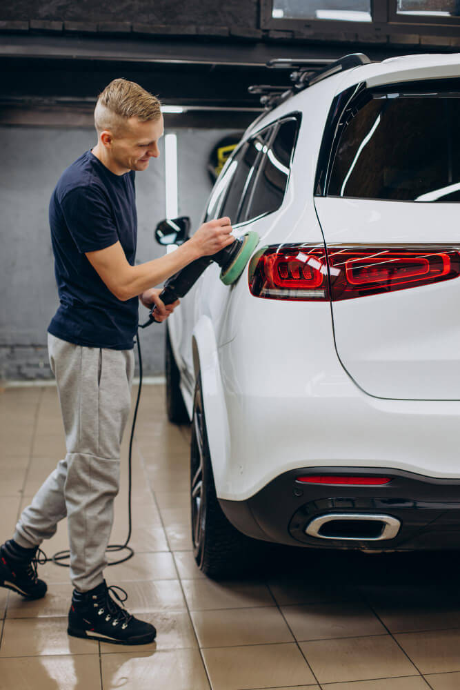 A worker polishing the back of a white SUV