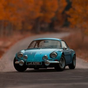 Blue classic sports car on a tree-lined autumn road