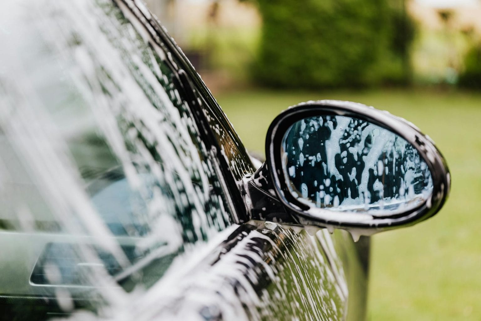 Black car door and side mirror covered in soap foam during a hand wash
