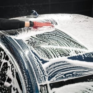 Gloved hand washing a foam-covered car roof with a microfibre wash mitt